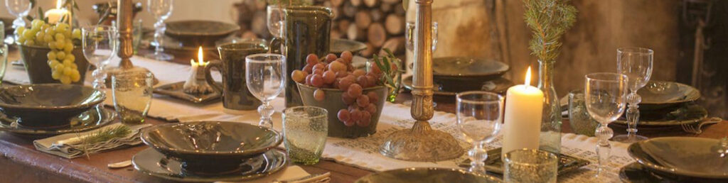 a dinner table setting with grapes in a bowl and lit candles