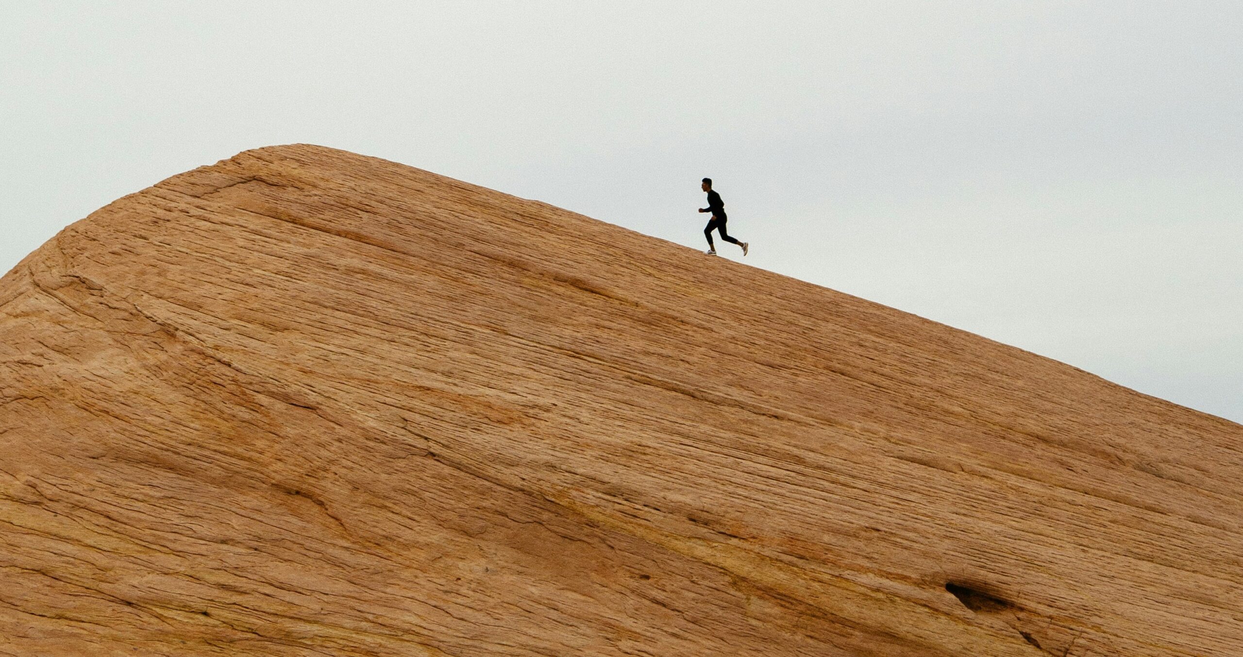 a person walking up a rock hill with a grey and blue sky in the background